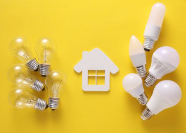 LED ve parlak ampuller ve sarı arka planda ev modeli. Elektrik tasarrufu