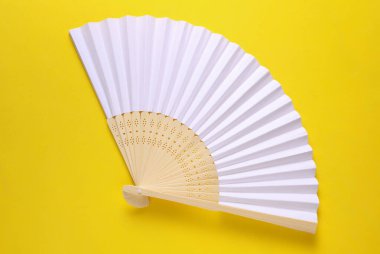 Sarı arka planda geleneksel beyaz Asyalı el vantilatörü.