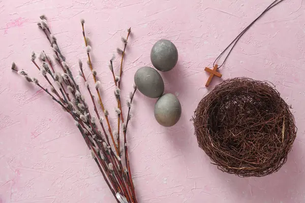 Easter eggs, nest with Christian cross and pussy willow branches on pink concrete background. Top view
