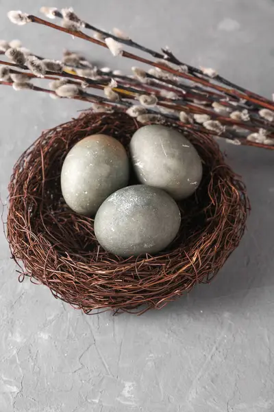 Easter eggs in nest with pussy willow branches on grey concrete background.