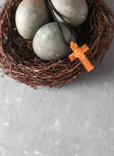 Yuvasında Paskalya yumurtaları ve gri beton arka planda Hıristiyan haçı.