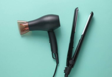 Modern siyah saç kurutma makinesi ve mavi arka planda saç ütüsü.