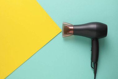 Mavi sarı arka planda modern siyah saç kurutma makinesi. Yaratıcı yerleşim