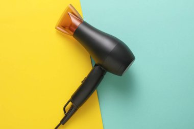 Mavi sarı arka planda modern siyah saç kurutma makinesi. Yaratıcı yerleşim