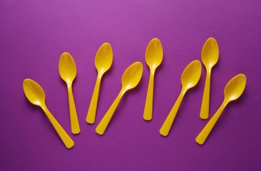 Mor arkaplanda sarı plastik kaşıklar.