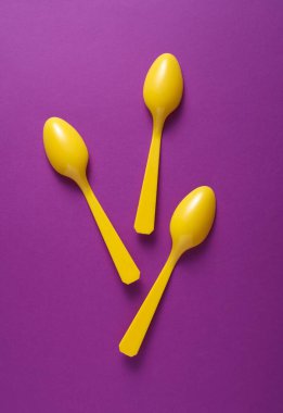 Mor arkaplanda sarı plastik kaşıklar.