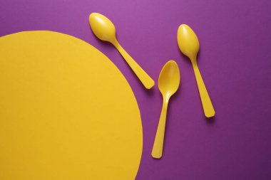 Sarı plastik kaşıklar mor arka planda sarı daireli. Yaratıcı yerleşim