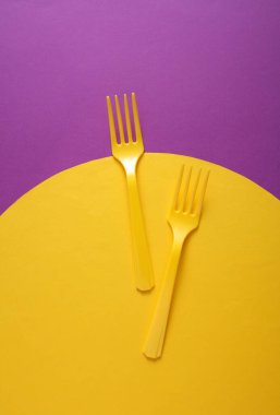 Sarı plastik çatallar mor arka planda ve sarı dairede. Yaratıcı yerleşim