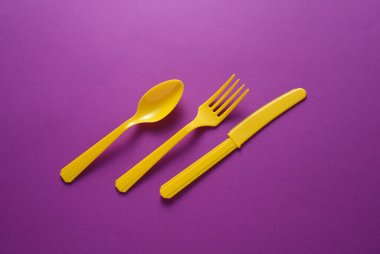 Sarı plastik çatal, mor arka planda bıçak ve kaşık.