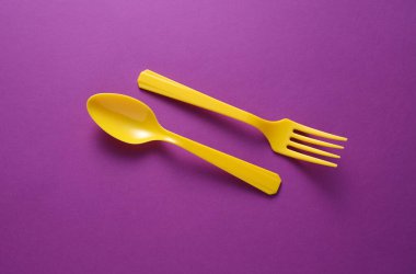 Sarı Plastik çatal ve kaşık mor arka planda.