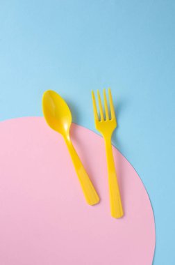 Mavi arka planda sarı plastik çatal ve kaşık. Yaratıcı yerleşim