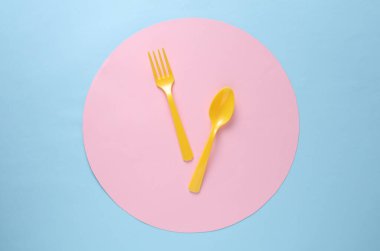 Sarı plastik çatal ve kaşık mavi arka planda pembe daireli. Yaratıcı yerleşim