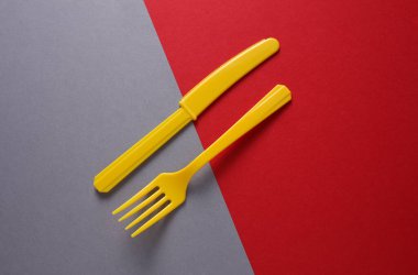 Sarı plastik çatal ve gri kırmızı arka planda bıçak. Minimalizm. Yaratıcı yerleşim