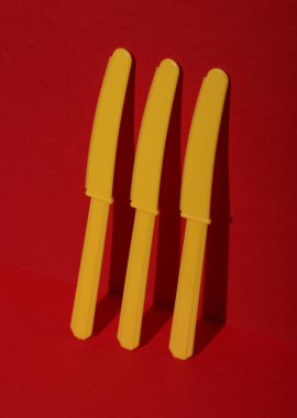 Kırmızı arka planda sarı plastik bıçaklar, gölgeli. Minimalizm. Yaratıcı düzen. Yiyecek konsepti