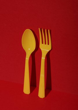 Sarı plastik kaşık ve çatal, kırmızı arka planda, gölgeli. Minimalizm. Yaratıcı düzen. Yiyecek konsepti