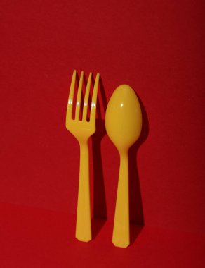 Sarı plastik kaşık ve çatal, kırmızı arka planda, gölgeli. Minimalizm. Yaratıcı düzen. Yiyecek konsepti