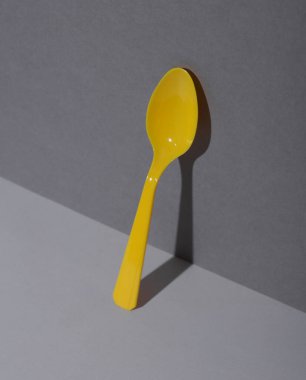 Gri arka planda gölgeli sarı plastik kaşık. Minimalizm. Yaratıcı düzen. Yiyecek konsepti