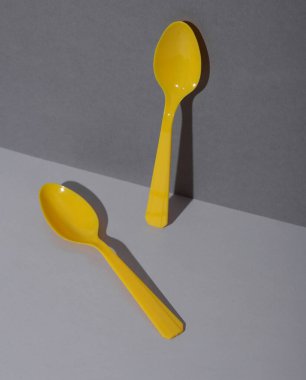 Gri arka planda gölgeli sarı plastik kaşıklar. Minimalizm. Yaratıcı düzen. Yiyecek konsepti