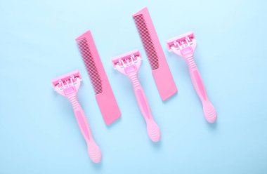 Kişisel hijyen eşyaları. Mavi arka planda pembe jiletler ve taraklar. Üst görünüm