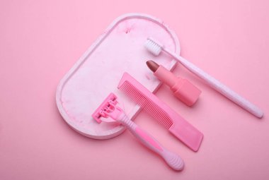 Kişisel hijyen eşyaları. Ustura ve tarak ile pembe diş fırçası, tepside ruj izi, mavi arkaplan.
