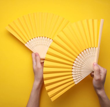 Sarı arka planda geleneksel Asyalı el vantilatörleri tutan eller