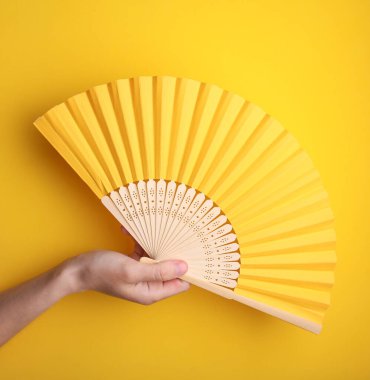 Sarı arka planda geleneksel Asyalı el tutuşan yelpaze.
