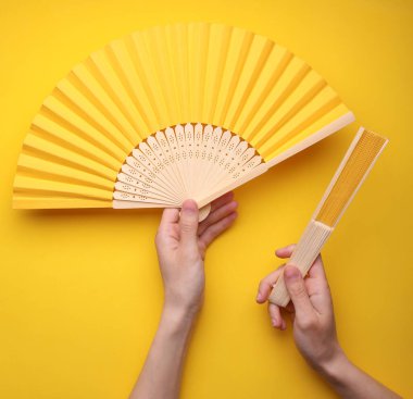 Sarı arka planda geleneksel Asyalı el vantilatörleri tutan eller