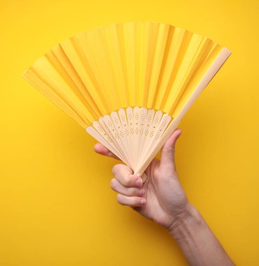 Sarı arka planda geleneksel Asyalı el tutuşan yelpaze.