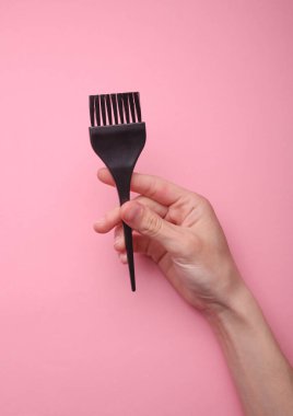 Pembe arka planda saç fırçası tutan el.