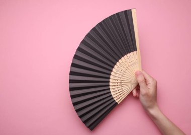 Pembe arka planda geleneksel Asyalı el tutuşan yelpaze.