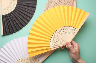 Mavi arka planda el ele tutuşan geleneksel Asyalı el yelpazesi