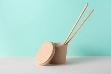 Sofrada yemek çubukları, turkuaz arka planda eko karton yemek kutusu.