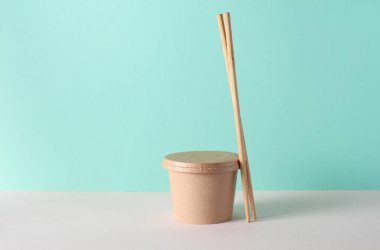 Sofrada yemek çubukları, turkuaz arka planda eko karton yemek kutusu.