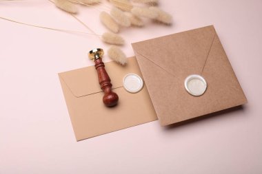 Balmumu mühürler ve vintage damgalı yüzen zarflar, bej arka planda kuru lagurular. Hediye çeki, düğün davetiyesi. Yaratıcı yerleşim