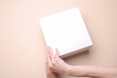 Kadın elleri bej arka planda beyaz karton kutuyu açıyor. Tasarım için maket. Üst görünüm