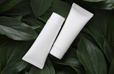 Yeşil bitki yaprakları üzerinde beyaz plastik krem tüpleri
