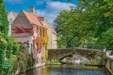 Bruges, Belçika - 18 Temmuz 2020: Geleneksel evler ve kanalda bir turist teknesi