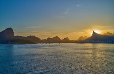 Brezilya, Rio De Janeiro, Rio 'nun ünlü körfezinin manzarası gün batımında denizden görülüyor.