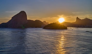 Brezilya, Rio De Janeiro, Rio 'nun ünlü körfezinin manzarası gün batımında denizden görülüyor.