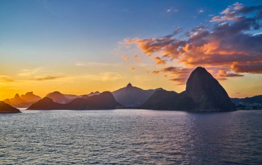 Brezilya, Rio De Janeiro, Rio 'nun ünlü körfezinin manzarası gün batımında denizden görülüyor.