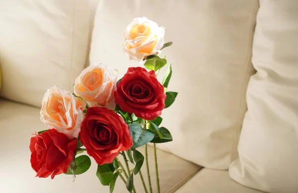 The picture shows a bouquet of red and pastel handmade fabric roses placed on a white sofa, close up.