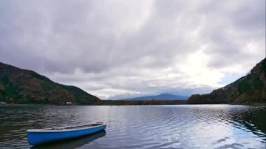 Teknesi, dağları ve hızla hareket eden bulutları olan gölün hızlandırılmış videosu. 