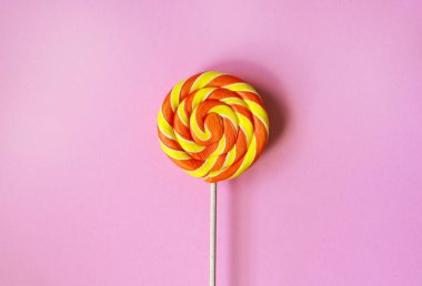 Tatlı Noel turuncu spiral lolipopu pembe arka planda. Çocukluk şekeri. Yuvarlak lezzetli tatlı.