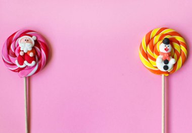 Noel çizgili pembe ve turuncu lolipoplar çubukların üzerinde. Pembe arka planda iki büyük yuvarlak lezzetli şeker. Şeker Noel Baba ve Kardan Adam. Üst Manzara. Boşluğu kopyala.