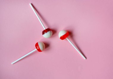 Üç pembe, kırmızı ve beyaz yuvarlak tatlı lolipoplar beyaz plastik çubuklar üzerinde pembe pastel arka planda.