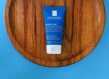 KYIV, UKRAINE - 8 Eylül 2022: La Roche Posay mini temizleme jeli efekti. Meşe ağacından bir tabakta plastik mavi tüp paketi. Mavi arka plan. Fransız kozmetik markası. Üst Manzara. Seçici odak.