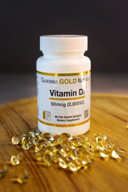 KYIV, UKRAINE - 15 Ekim 2022: Kaliforniya Altın Beslenme Vitamini D350 mcg takviye. Sarı balık jelatin yumuşak sebze kapsülleri. Ahşap ve karanlık arka plan. Seçici odak.