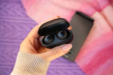 Suçlama davasında siyah kulaklık takan bir kadın. Örülmüş mor ve pembe arka plan. Siyah paket kablosuz kulaklık. Seçici odak.