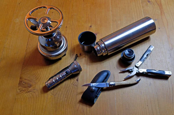 Still life of outdoor gear: Stove, thermos, flashlight, knife and multitool