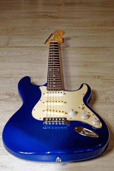 Music, pop, rock: Blue electric guitar, Stratocaster shape, against a white background with a wooden struc-ture
